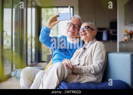 Heureux couple senior assis sur le canapé à la maison prenant selfie Banque D'Images