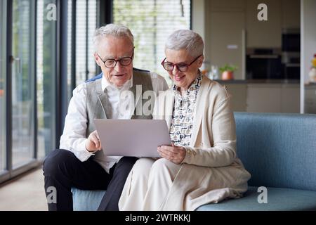 Couple senior assis sur le canapé à la maison à l'aide d'une tablette PC Banque D'Images