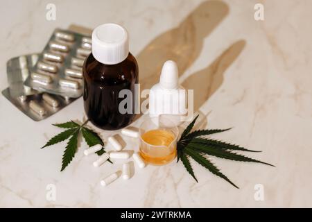 Maquettes de médicaments sur un fond beige avec des feuilles de cannabis. Dispositions d'une bouteille brune, un flacon pulvérisateur blanc, de l'huile et des pilules sur une table en marbre avec Banque D'Images