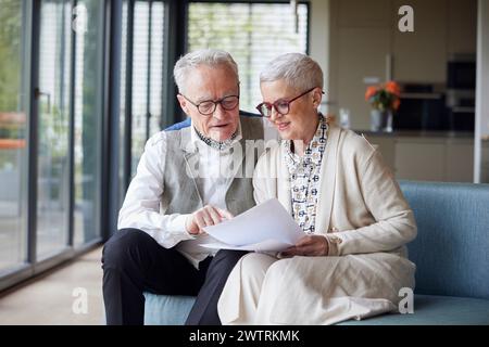 Couple senior assis sur le canapé à la maison lisant le document Banque D'Images