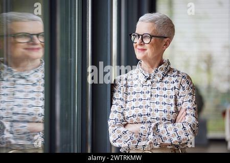 Femme senior à la maison regardant par la fenêtre Banque D'Images