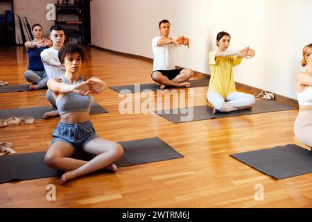 Les personnes athlétiques de différents âges et races pratiquent des asanas de yoga avec un entraîneur. Jeunes femmes et hommes sportifs multiethniques assis les jambes croisées sur des tapis, regardez un Banque D'Images