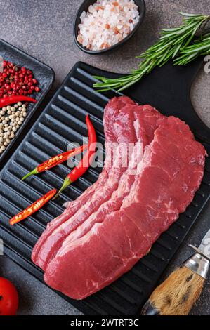 bacon de bœuf marbré. planche à découper en bois noir avec bacon de bœuf marbré cru et assaisonnements, plat sur fond de pierre taupe. Banque D'Images