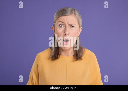 Portrait de femme senior surprise sur fond violet Banque D'Images