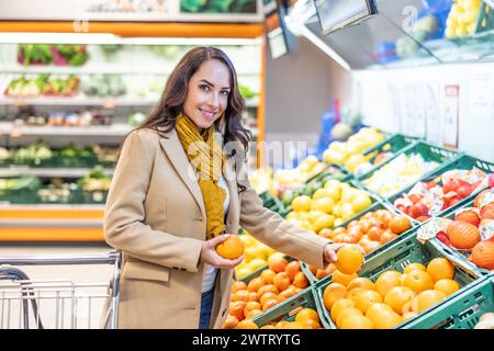Woman shopping for groceries with a shopping cart. A young brunette buys fruit in a supermarket. Banque D'Images
