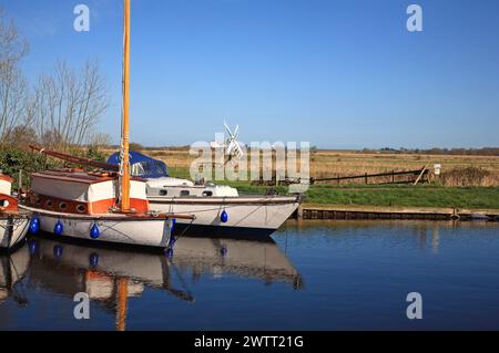 Une vue sur les marais de Bure avec des bateaux amarrés, des reflets et des moulins à vent sur les Norfolk Broads depuis la Staithe à Upton, Norfolk, Angleterre, Royaume-Uni. Banque D'Images