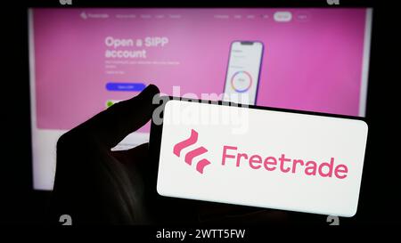 Personne tenant un smartphone avec le logo de la société fintech britannique Freetrade Ltd. en face du site Web. Concentrez-vous sur l'affichage du téléphone. Banque D'Images