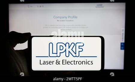 Personne tenant le téléphone portable avec le logo de la société de technologie allemande LPKF laser Electronics se en face de la page Web de l'entreprise. Concentrez-vous sur l'affichage du téléphone. Banque D'Images