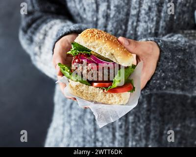 Gros plan des mains tenant un hamburger juteux prêt à manger. Banque D'Images