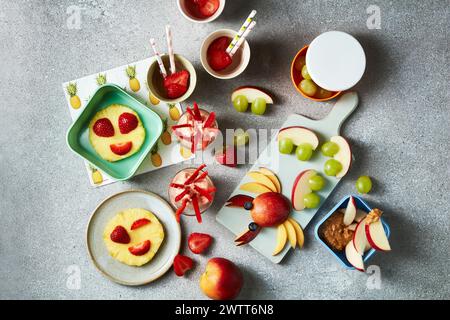 Un affichage coloré de collations saines avec des visages de fruits sur un fond gris texturé. Banque D'Images