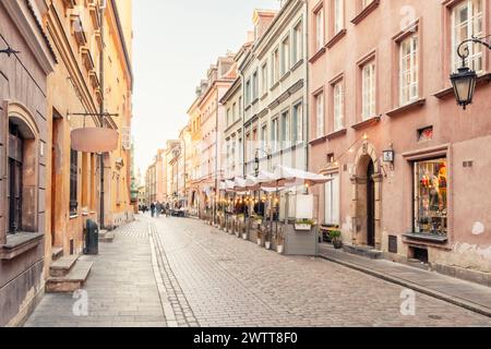 Rue pavée baignée d'une douce lueur chaude au coucher du soleil, bordée de boutiques pittoresques et de restaurants dans une ville européenne historique. Banque D'Images