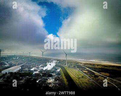 Une vue aérienne sombre d'une zone industrielle côtière avec des éoliennes et des nuages spectaculaires. Banque D'Images