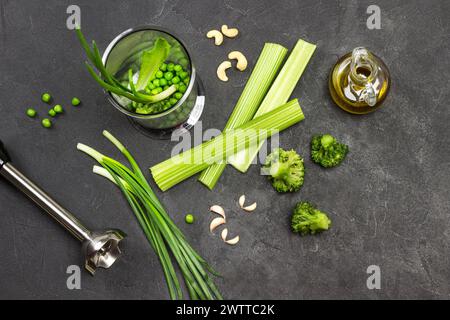 Ensemble de légumes sur la table et dans le bol du blender. Bouteille d'huile d'olive. Tiges de céleri et oignons verts. Noix de cajou et ciboulette. Brocoli et pois verts. Bla Banque D'Images