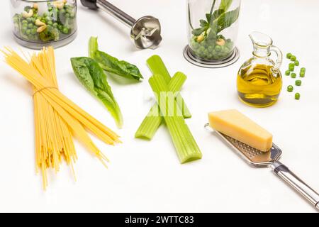 Pâtes et parmesan sur râpe. Bol du blender avec légumes. Tiges de céleri et laitue romaine. Bouteille d'huile d'olive. Vue de dessus. Fond blanc. Banque D'Images