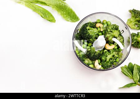 Pois verts, brocoli et noix de cajou dans un bol mélangeur. Salade romaine et menthe sur table. Copier l'espace. Vue de dessus. Fond blanc. Banque D'Images