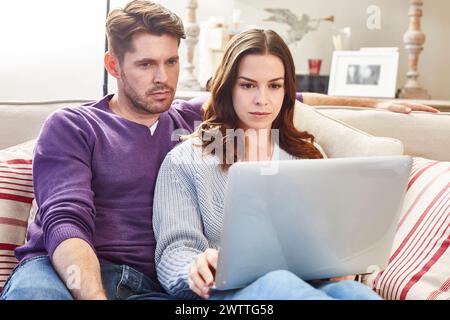 Couple assis sur un canapé à l'aide d'un ordinateur portable. Banque D'Images