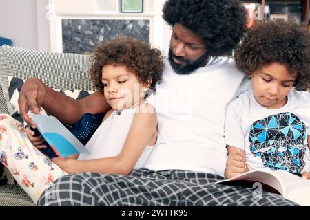 Père lisant un livre avec deux enfants sur un canapé Banque D'Images