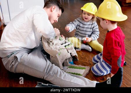 Adulte jouant avec deux enfants portant des casques de jouet Banque D'Images