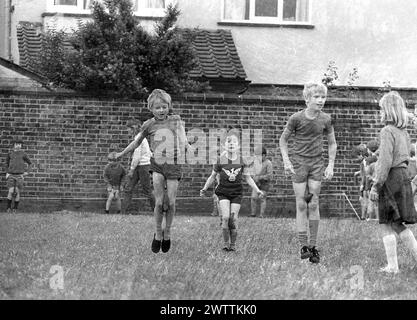 Années 1970, historique, sport à l'école primaire, dehors dans un champ d'herbe, de jeunes enfants prenant part à une course de saut tenant une éponge entre leurs genoux, Angleterre, Royaume-Uni. Banque D'Images