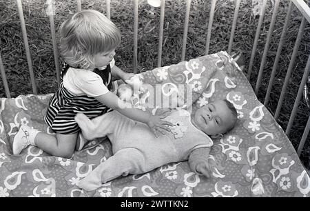 Années 1970, historique, à l'intérieur d'un parc en bois, une petite fille interagissant avec son petit frère allongé sur le dos regardant vers le haut, Angleterre, Royaume-Uni. Banque D'Images