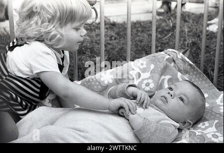 Années 1970, historique, une petite fille avec son petit frère allongé sur le dos dans un parc en bois, tenant la petite main de l'enfant, Angleterre, Royaume-Uni. Banque D'Images