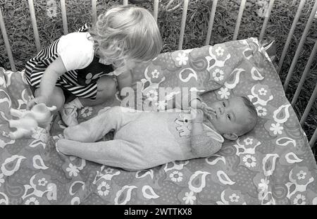 Années 1970, historique, une petite fille avec son petit frère allongé dans son parc, Angleterre, Royaume-Uni. Banque D'Images