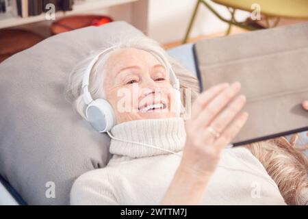 Femme âgée avec des écouteurs à l'aide d'une tablette Banque D'Images