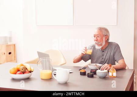 Homme senior prenant le petit déjeuner et utilisant un ordinateur portable Banque D'Images