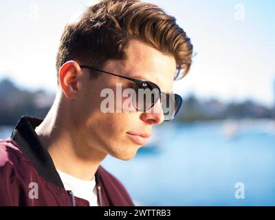 Jeune homme portant des lunettes de soleil près de l'eau. Banque D'Images