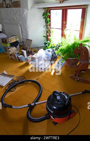 Vue verticale de l'intérieur de la chambre avec fenêtre, plantes d'intérieur Henry aspirateur livres tapis ressort nettoyage à l'intérieur de la maison chalet UK 2024 KATHY DEWITT Banque D'Images