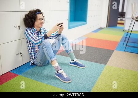 Personne souriante assise sur le sol à l'aide d'un smartphone Banque D'Images