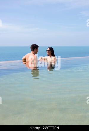 Couple profitant d'une piscine à débordement surplombant l'océan Banque D'Images