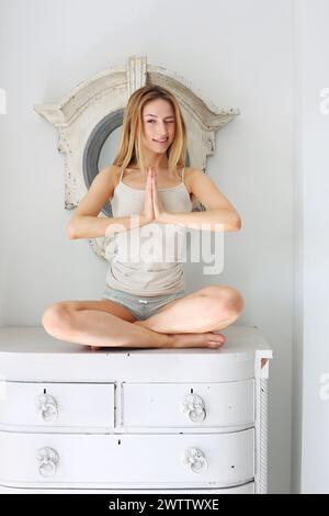 Femme pratiquant le yoga sur une commode blanche Banque D'Images