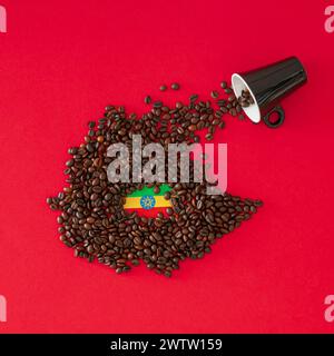 Composition créative faite avec tasse de café, carte de l'Ethiopie faite avec des grains de café torréfiés et drapeau éthiopien sur fond rouge. Disposition minimale. Banque D'Images