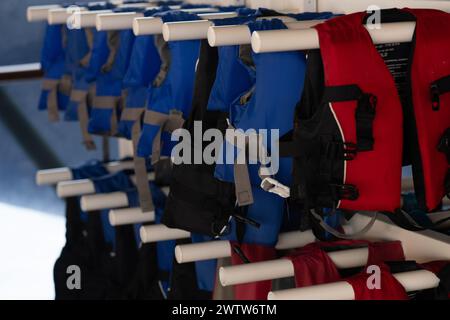 Une rangée de gilets de sauvetage bleus et noirs accrochés sur des supports blancs, essentiels pour la sécurité de l'eau et la préparation aux situations d'urgence Banque D'Images