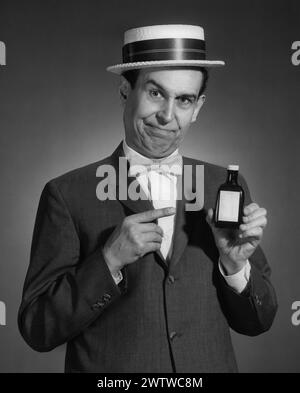 Portrait d'un homme dans un costume de chapeau de paille et noeud papillon tenant une bouteille de médicament dans une main, l'autre main pointant vers la bouteille alors qu'il donne son argumentaire de vente Banque D'Images