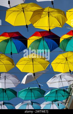 Un ensemble de parapluies aux couleurs vives suspendus au-dessus d'un ciel bleu clair créant une verrière festive Banque D'Images