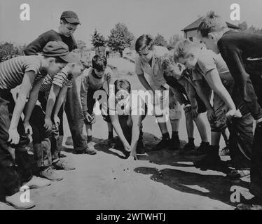 Grand groupe de garçons d'âge scolaire dans un caucus autour d'une fosse de marbre de terre jouant des billes Banque D'Images