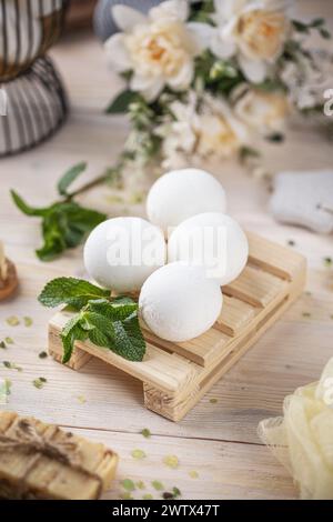 Élégantes bombes de bain disposées sur un plateau en bois orné de menthe fraîche et de doux fond floral Banque D'Images