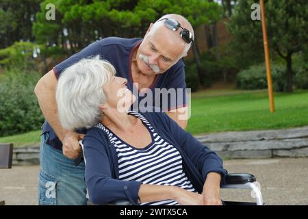 couple mûr dehors femme marchant dans un fauteuil roulant Banque D'Images