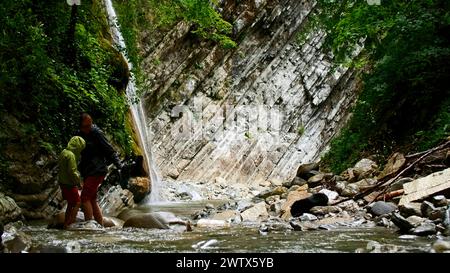 Belle cascade dans la forêt verdoyante. Créatif. Mère et garçon traversant une rivière tropicale dans la jungle de montagne. Banque D'Images