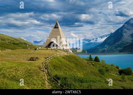 Vue sur l'église moderne en forme de pyramide, le lac alpin du Mont-Cenis et les montagnes sur fond en France. Banque D'Images