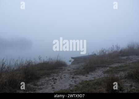 Sentier boueux mène au bateau amarré dans le brouillard, calme soirée brumeuse près de la rivière, navire nautique Banque D'Images