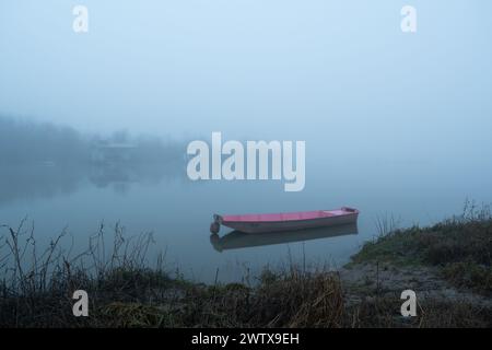 Sentier boueux mène au bateau amarré dans le brouillard, calme soirée brumeuse près de la rivière avec des cabanes de pêche sur l'île, navire nautique Banque D'Images