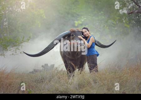 Portrait d'une femme debout dans un champ caressant un buffle d'eau, Thaïlande Banque D'Images