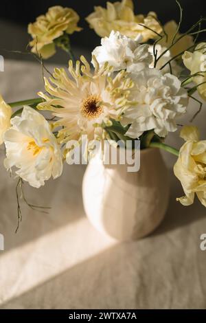 Bouquet de gerbera jaune, tulipe et fleurs de ranoncule dans un vase sur une table au soleil Banque D'Images