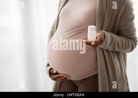 Jeune femme noire enceinte méconnaissable tenant un pot avec des pilules Banque D'Images