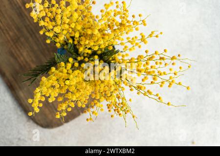 Vue aérienne d'un bouquet de tiges de mimosa jaune dans un vase sur une planche à découper en bois Banque D'Images
