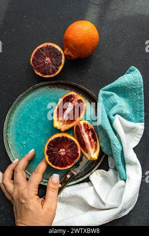 Vue aérienne d'une femme atteignant des oranges sanguines sur une assiette avec une serviette Banque D'Images
