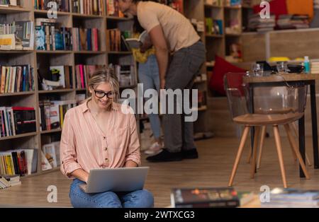 Portrait d'une jeune étudiante assise à la bibliothèque à l'aide d'un ordinateur portable avec ses amis en arrière-plan. Banque D'Images